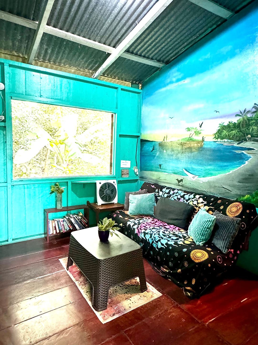 Turquoise lounge with a painted Caribbean beach mural, a patterned futon and a big window
