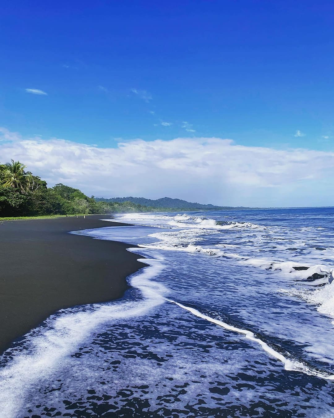 Playa Negra: white foam on dark sand with green hills in the distance