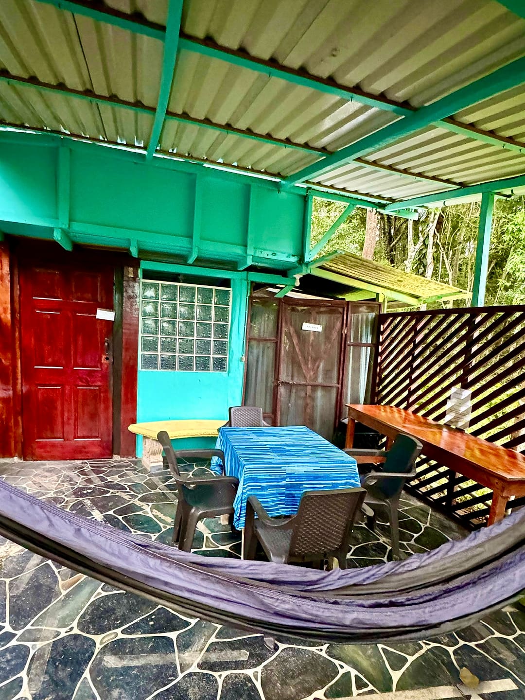 Patio dining table with a blue cloth, a hammock and red doors on a flagstone floor