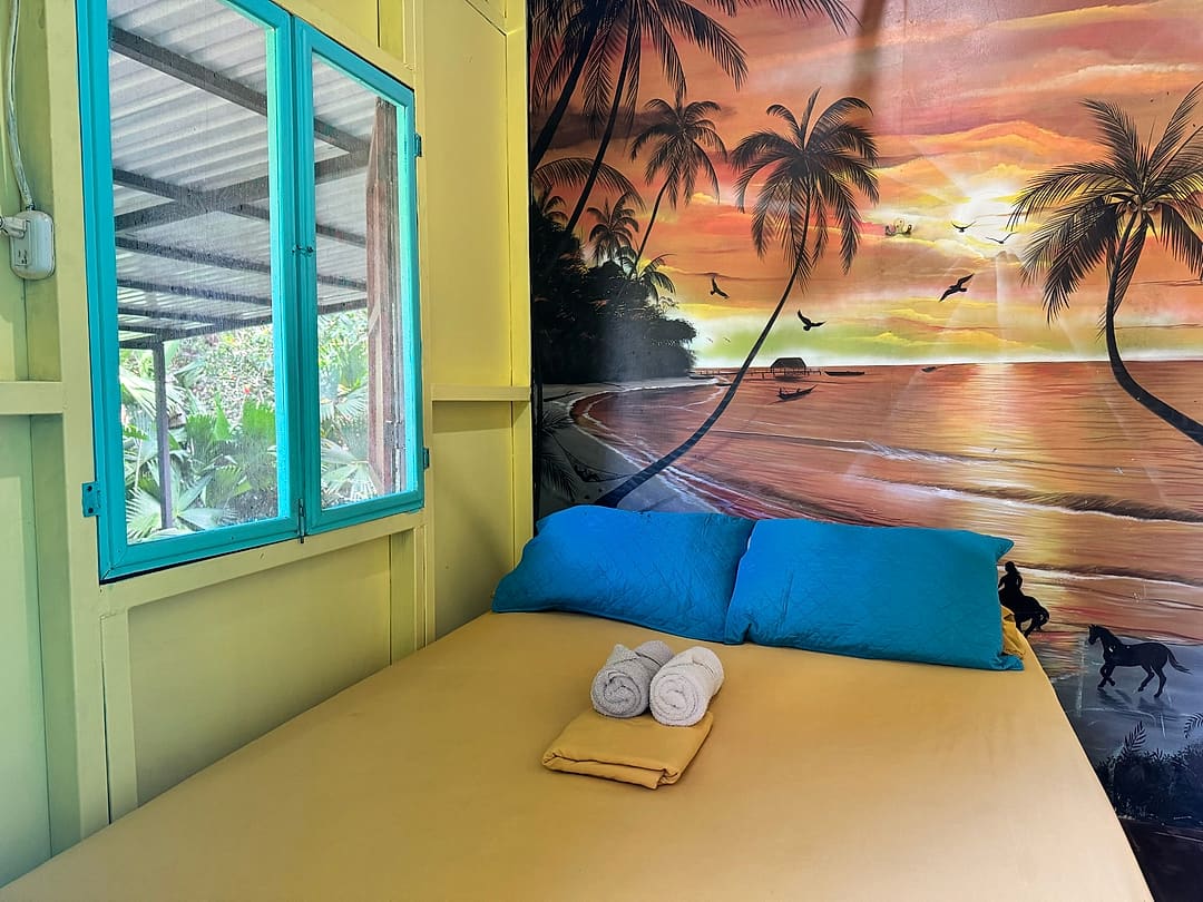 Sunshine Room 3: yellow bed with blue pillows below a painted sunset-beach mural