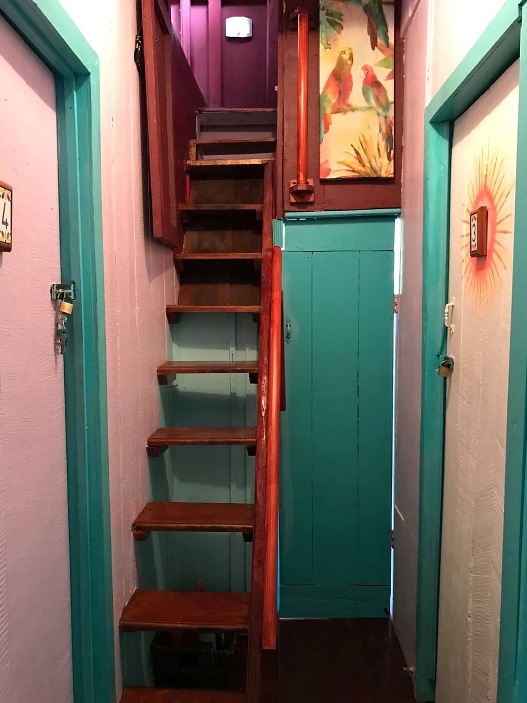 The steep, narrow wooden staircase up to the Treetop Balcony Room, between painted hallway doors