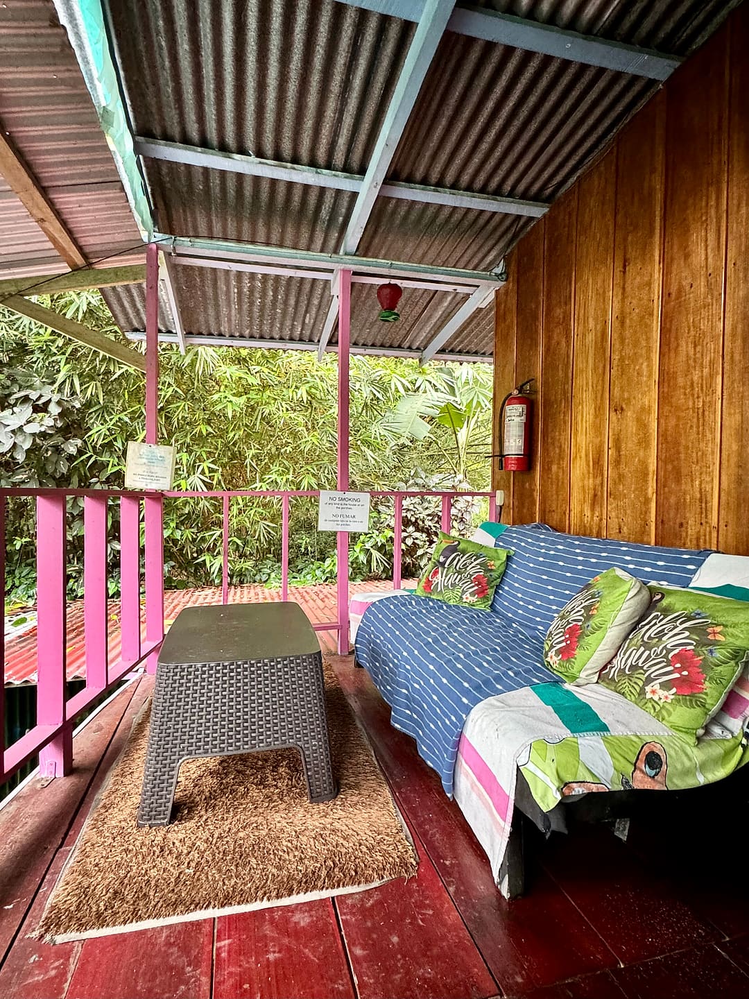Covered upper terrace with pink railings, a striped sofa and cushions facing the jungle